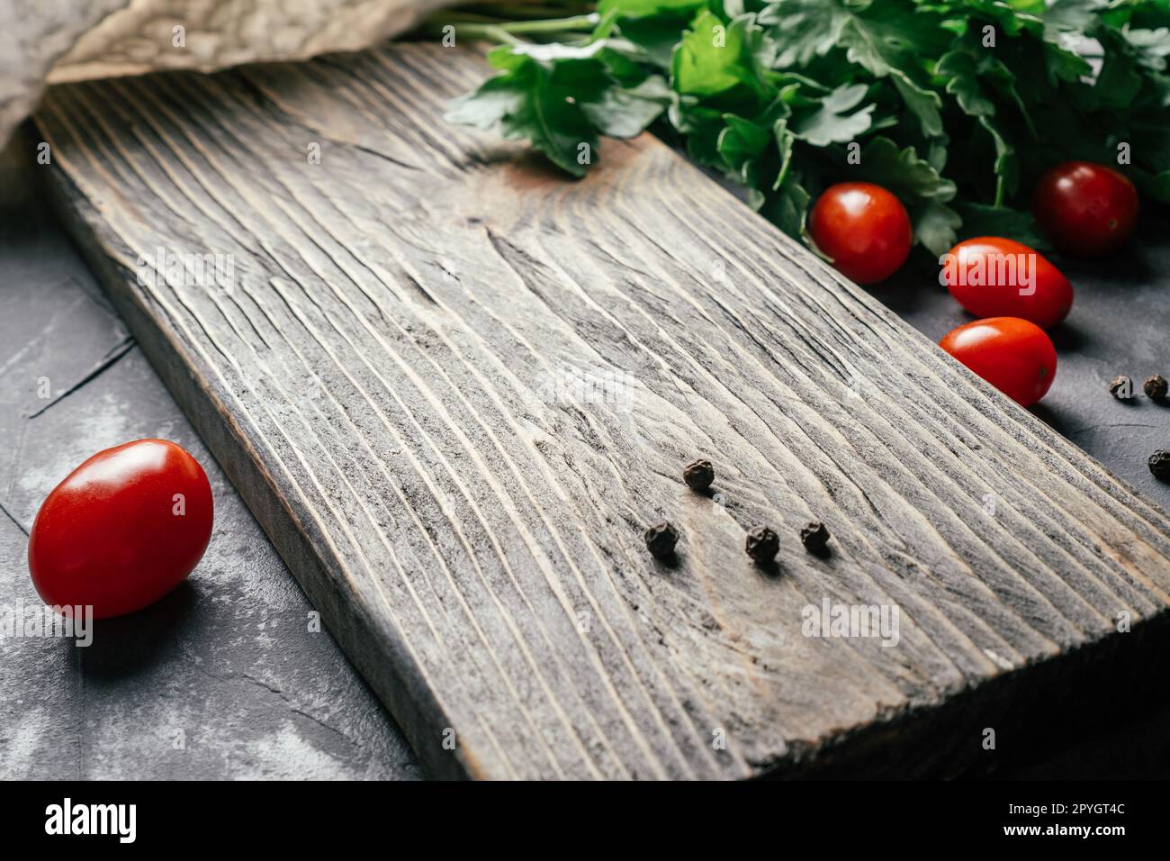 Tagliere testurizzato su superficie in calcestruzzo grigio con pomodori ciliegini, prezzemolo e pepe in grani, concetto di cucina Foto Stock