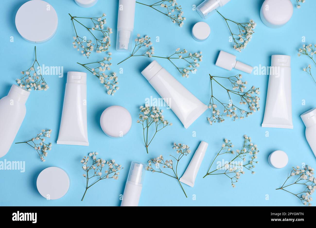 Tubi, vasetti e rami di gypsophila bianchi su sfondo blu, contenitori per creme e gel cosmetici, pubblicità e promozione del marchio Foto Stock