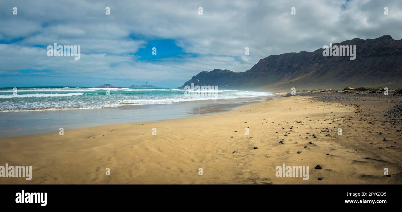 Vista sulla spiaggia di Famara sull'Isola Canaria di Lanzarote, con un po' di windsurf in lontananza Foto Stock