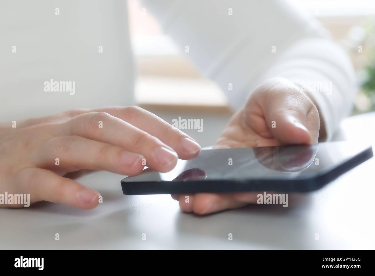 Mani di una giovane donna che utilizza l'app online sul telefono cellulare, effettuare chiamate, navigare in Internet, chattare sui social media, tenere il cellulare, inviare SMS, digitare messaggi. Primo piano su una scrivania bianca dai colori luminosi Foto Stock