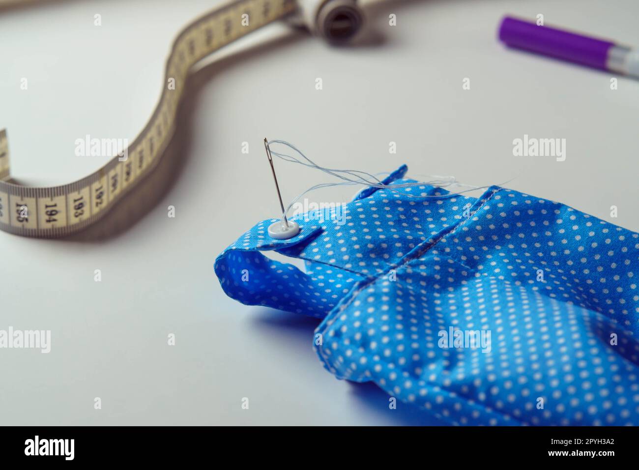 Piccolo e carino costume a pois blu con tuta da ginnastica per giocattolo vicino al metro a nastro e penna su tavolo bianco. Cucito Foto Stock