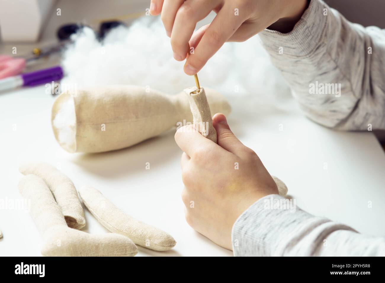 Primo piano le mani di sarta femminili irriconoscibili che cucono giocattoli morbidi, riempiti di cotone sul tavolo in officina. Negozio per bambini Foto Stock
