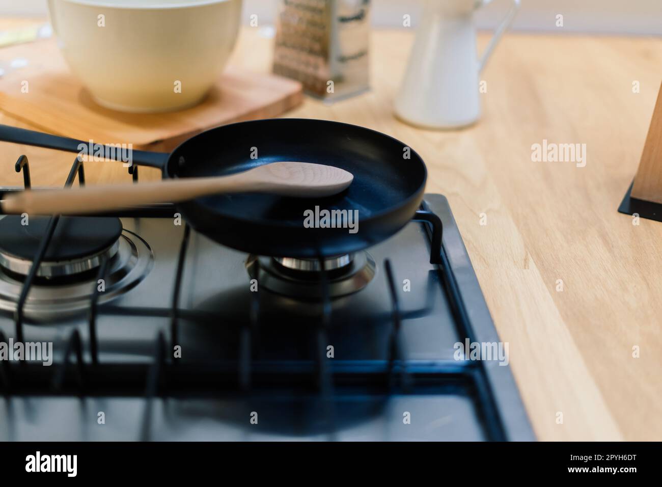 Spatola in padella teflon su piano cottura a gas contro il cucchiaio appeso in una piccola cucina Foto Stock