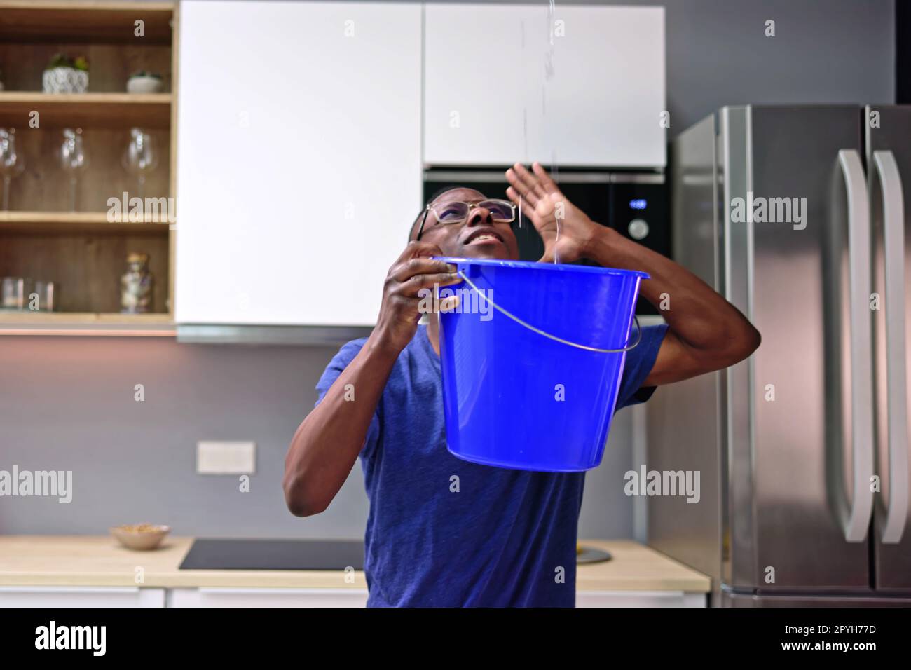 Uomo preoccupato che tiene il secchio mentre perde acqua dal soffitto Foto Stock