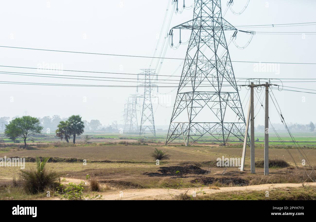 Linee elettriche su un campo agricolo contro l'orizzonte del cielo chiaro. Torre ad alta tensione installata in fila su un campo. Foto Stock