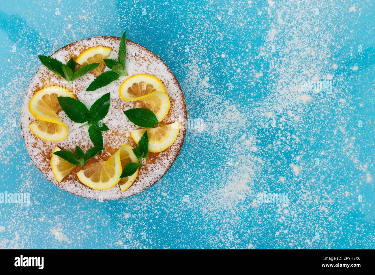 Torta di limone con fette di limone, menta e zucchero in polvere su sfondo blu. Vista dall'alto. Copia spazio. Foto Stock