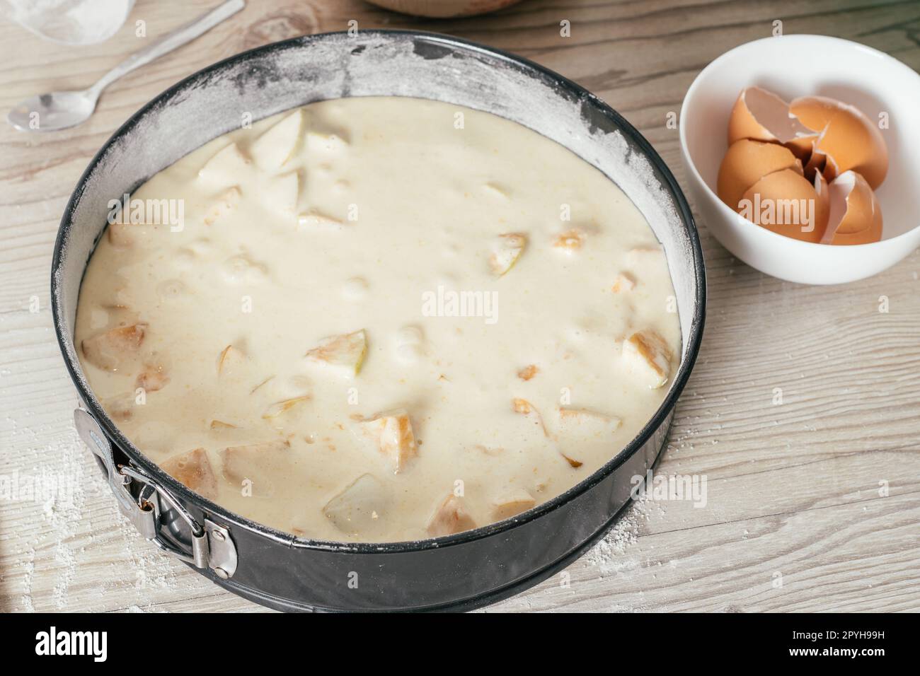 Il piatto da forno con impasto crudo di torta di mele si trova sul bancone della cucina accanto al recipiente con gusci d'uovo Foto Stock