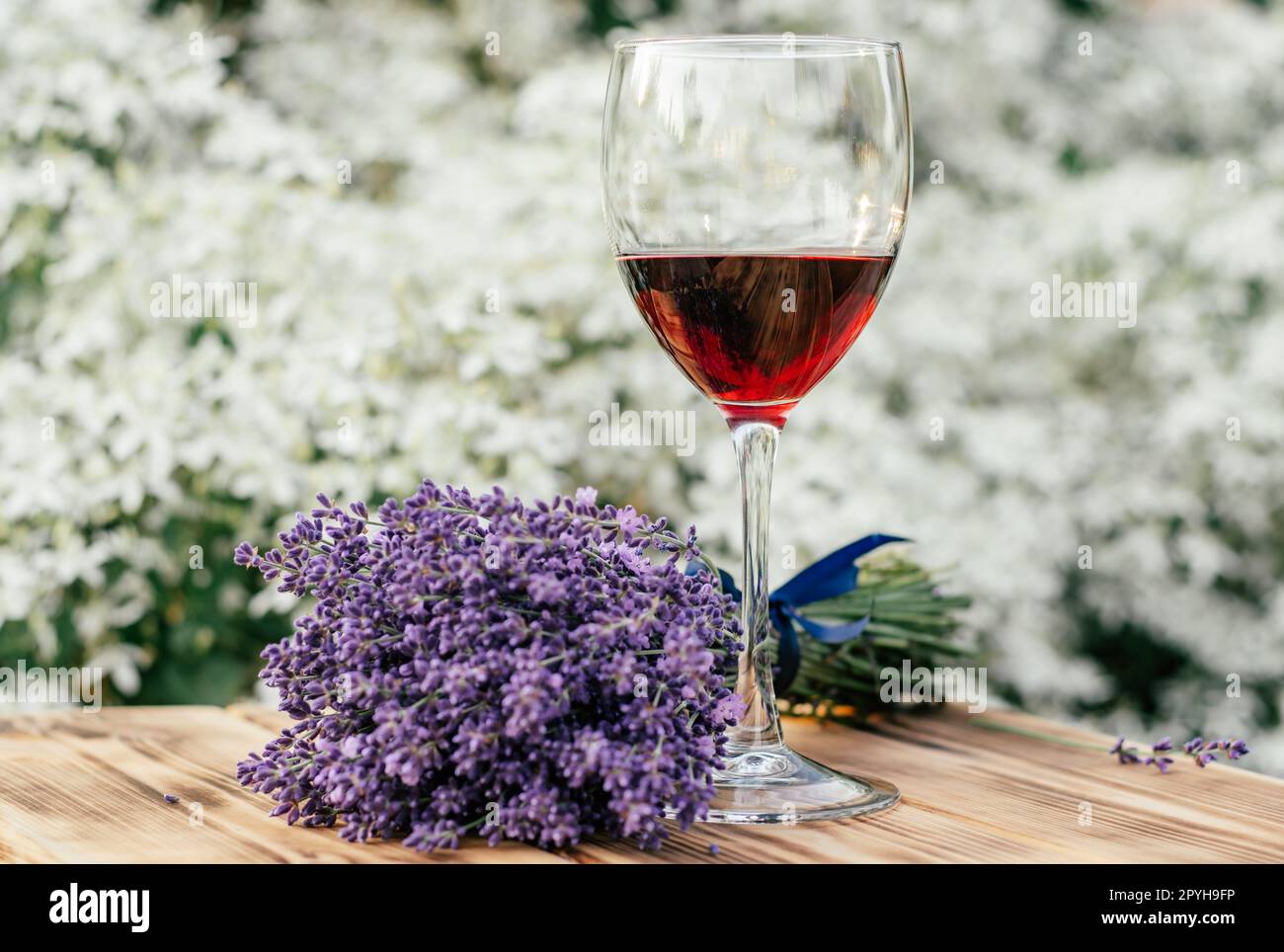 Bicchiere di vino pieno di boccioli di fiori di rosa essiccati che si  trovano sul tavolo blu.