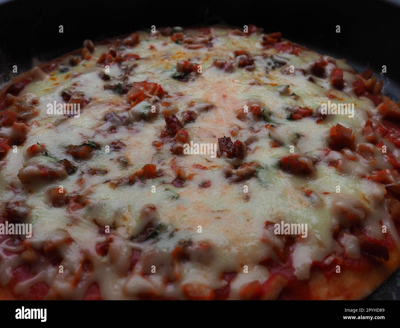 primo piano sulla pizza intera. Deliziosa pizza rotonda succosa con pomodori e salame. Il formaggio fuso viene versato sulla superficie della torta al forno. Controluce. Messa a fuoco morbida e sfocata Foto Stock