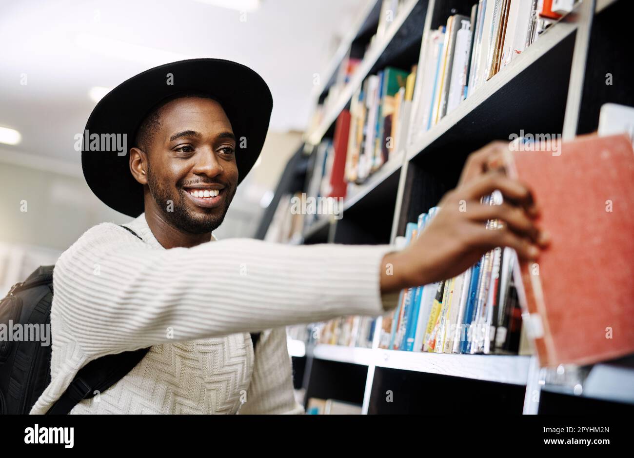 HES è sempre stato un lettore esigente. un giovane uomo felice che rimuove un libro da una mensola in una biblioteca dell'università. Foto Stock