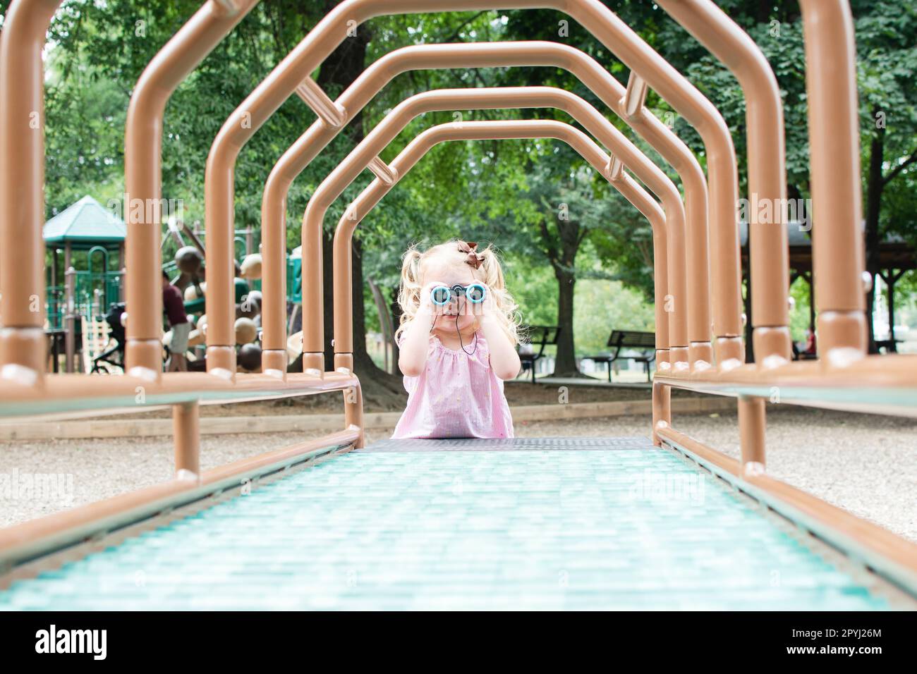 Carina ragazza caucasica bambino guardando attraverso binocoli sul parco giochi. Esplorazione del concetto Foto Stock