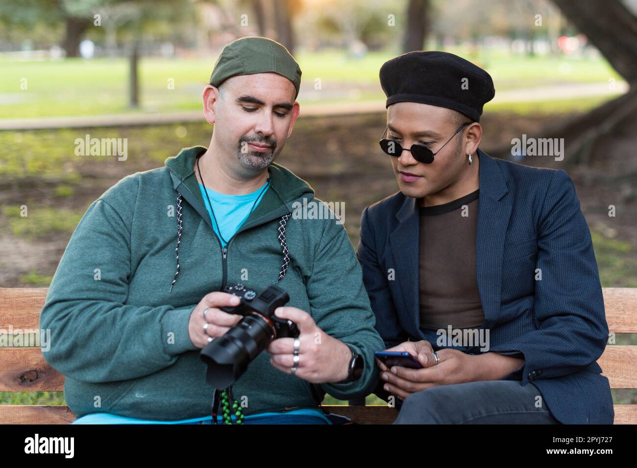 Coppia gay che parla e cerca un menu macchina fotografica mentre si siede  su una spiaggia in un parco. Uno di loro sta guardando la fotocamera Foto  stock - Alamy