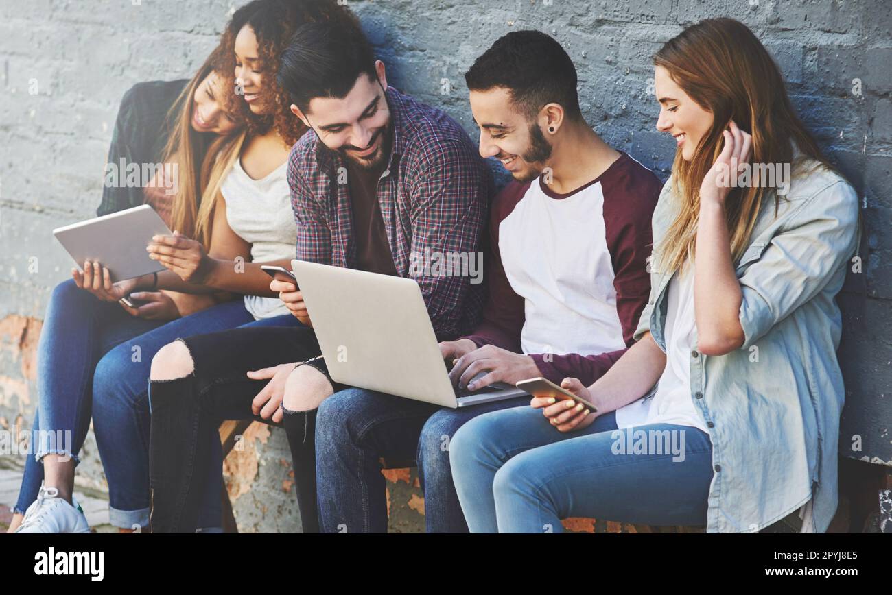 Socializzare online e in tempo reale. un gruppo di giovani amici che utilizzano i loro dispositivi wireless insieme all'aperto. Foto Stock