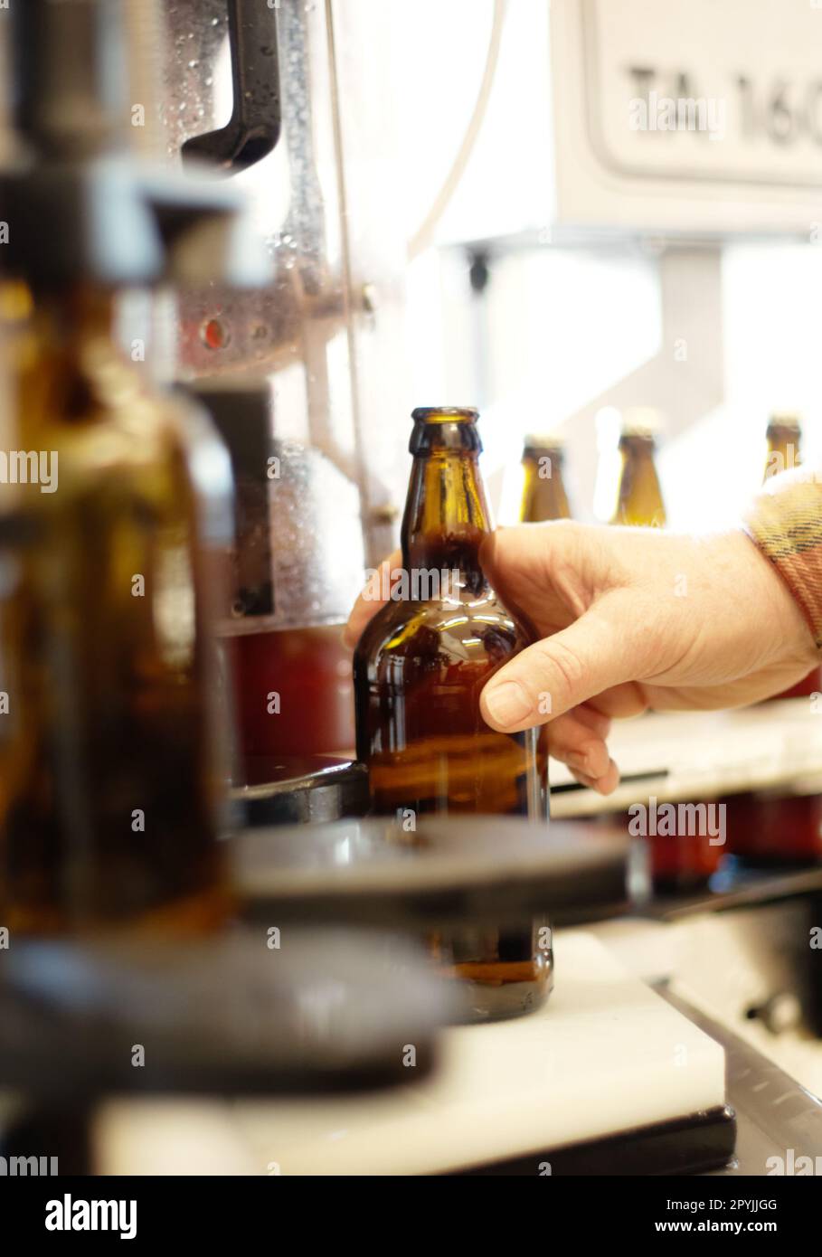 Mani, birra e bottiglia in fabbrica, birreria o impianto di produzione per l'ispezione della qualità. Alcool, linea di produzione e persona che prende il vetro da Foto Stock