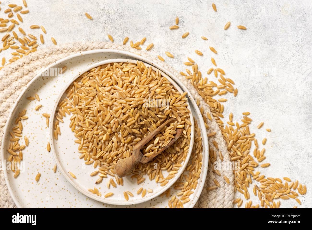 Piatto di grano di segale secco crudo con cucchiaio di legno sulla vista bianca del piano d'esame Foto Stock
