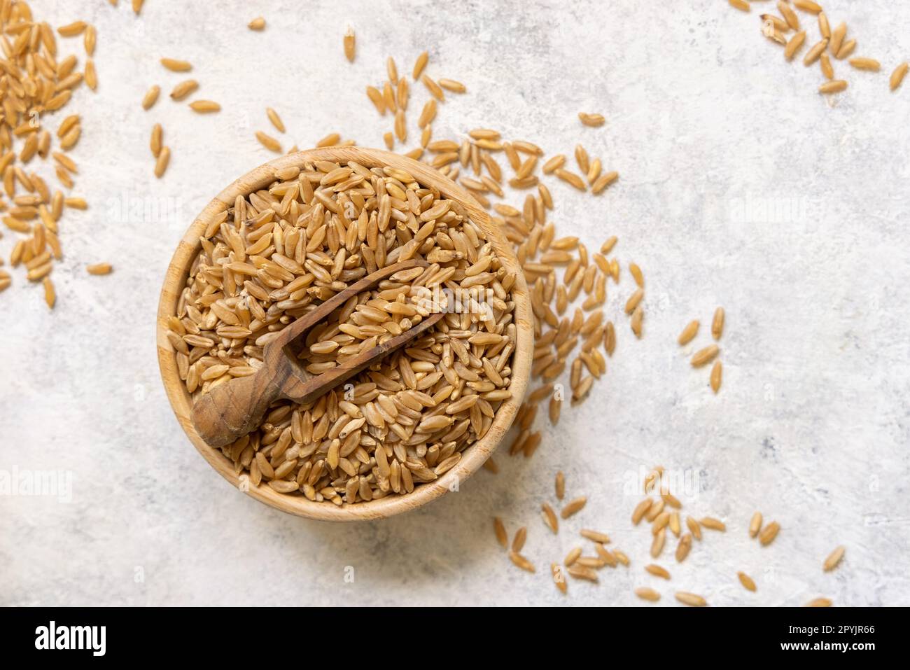 Recipiente di grano di segale secco crudo con cucchiaio di legno sulla vista bianca del piano d'esame Foto Stock