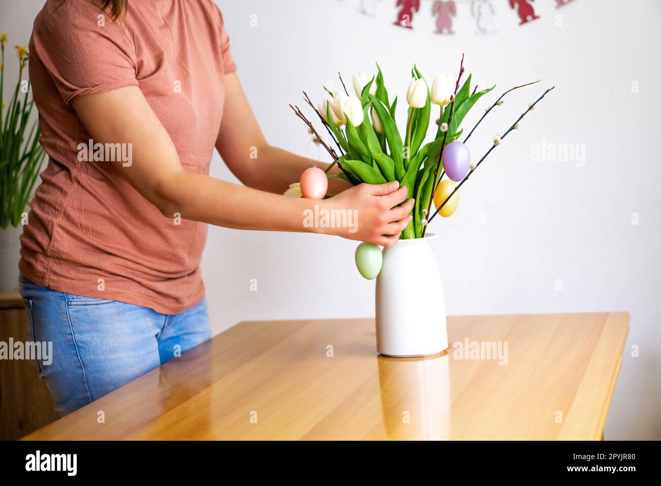 Mani femminili da fioraio che decorano un bouquet di brunch salice con uova di Pasqua colorate a casa. Foto Stock