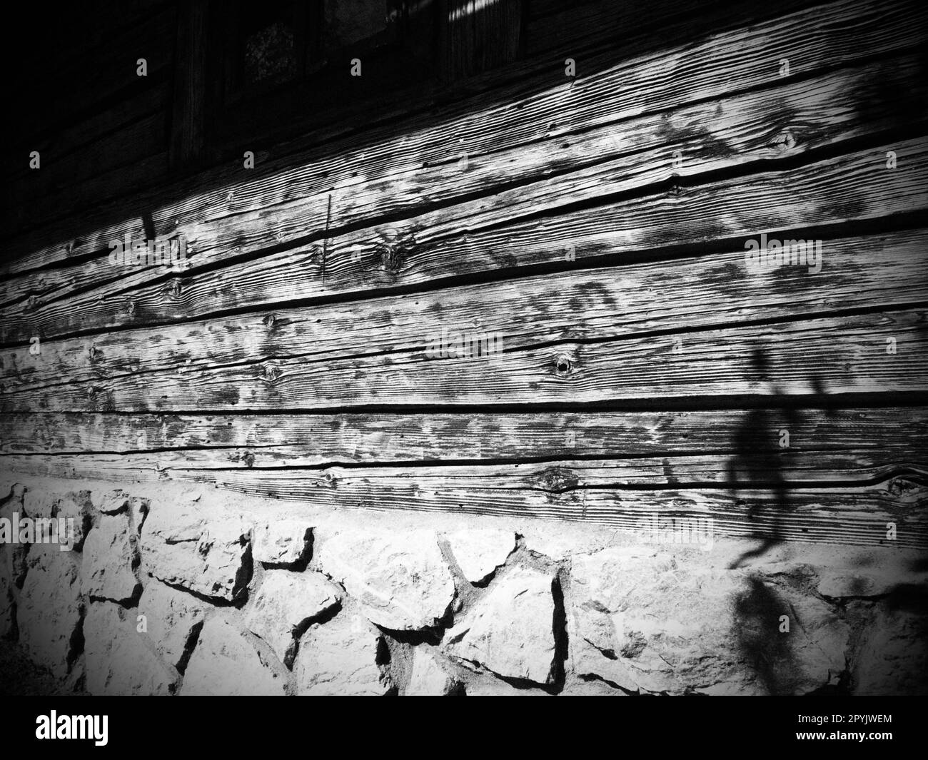 Muro in legno di legno di una vecchia casa di villaggio. Fondamenta acciottolate. Vecchi metodi di costruzione di edifici residenziali. Fotografia in bianco e nero, monocromatica Foto Stock