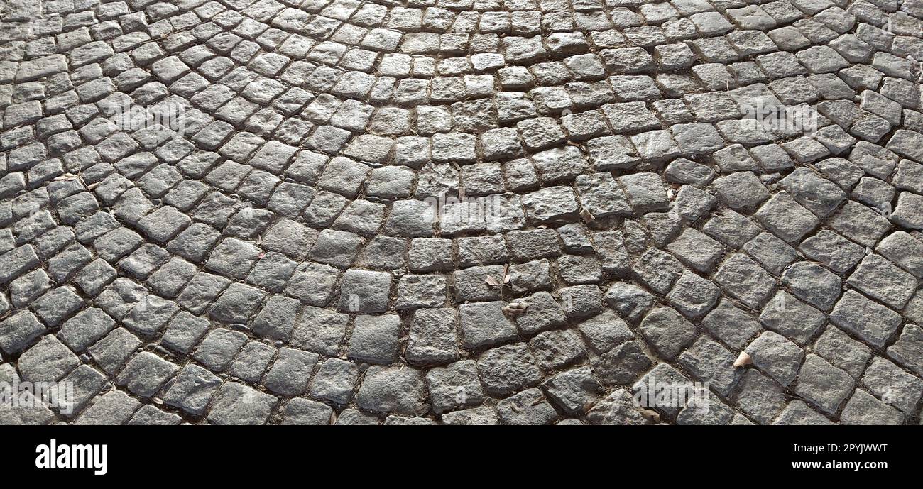 Antico marciapiede. Marciapiede fatto di pietre grigie. Ciottoli sulla piazza della città vecchia. Piastrelle irregolari disposte in cerchio. Struttura in pietra naturale Foto Stock