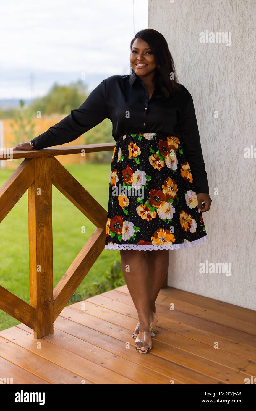 Donna afro-americana che si rilassa e si gode il sole in terrazza o sul balcone alla luce del sole d'estate. Vita lenta, momento tranquillo e salute mentale. Fine settimana di vacanza con terrazza sul retro. Cottagecore e inclusione con diversità Foto Stock