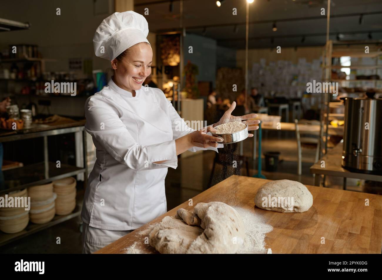 Donna panettiere in uniforme semina la farina attraverso il setaccio da cucina sulla pasta Foto Stock