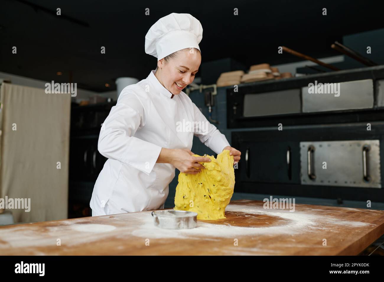 Felice donna sorridente fornaio pezzo di pasta tagliata con coltello su tavolo di legno Foto Stock