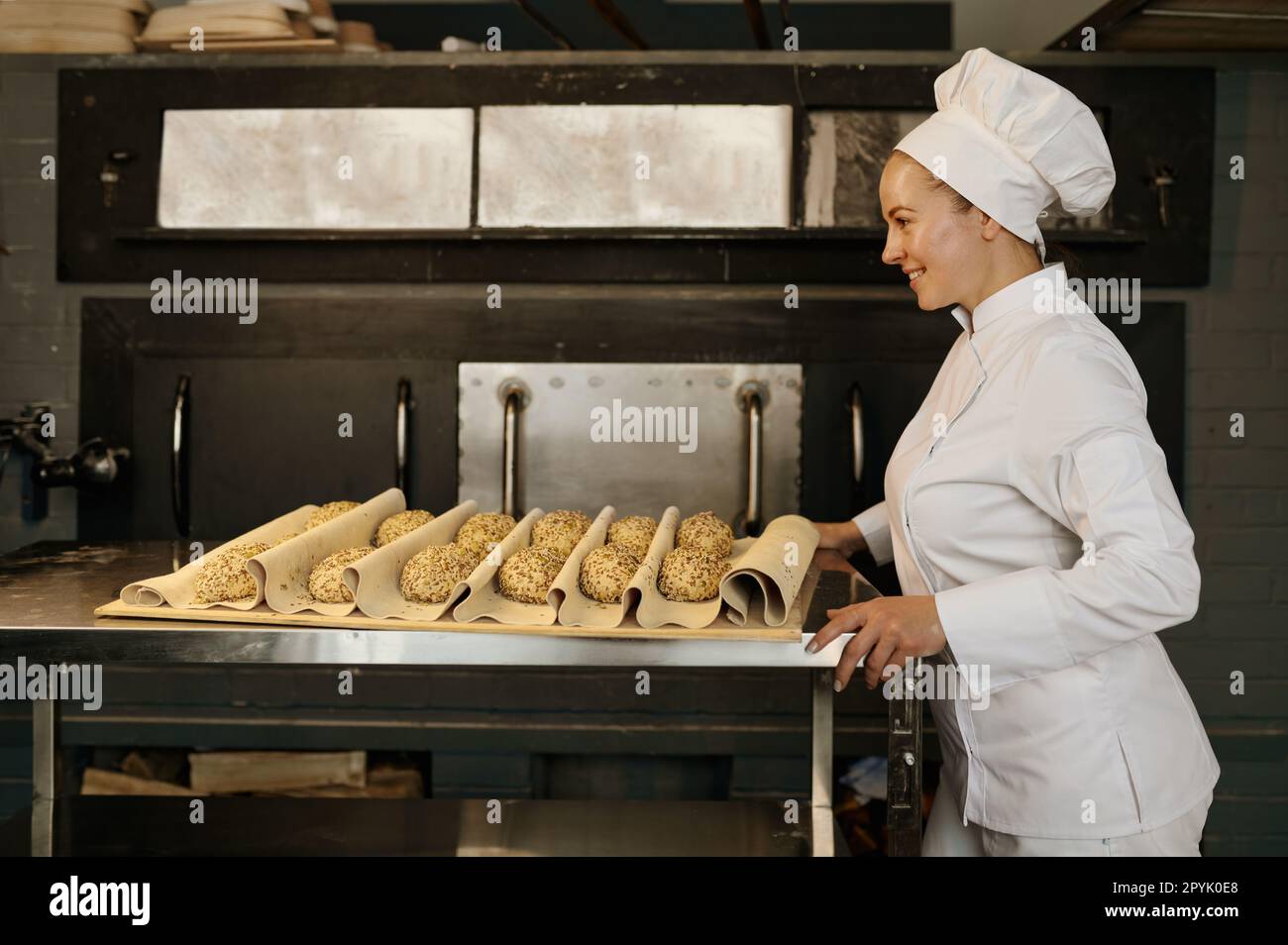 Panettiere che tira un vassoio con panini crudi con semi di sesamo preparati per la cottura Foto Stock