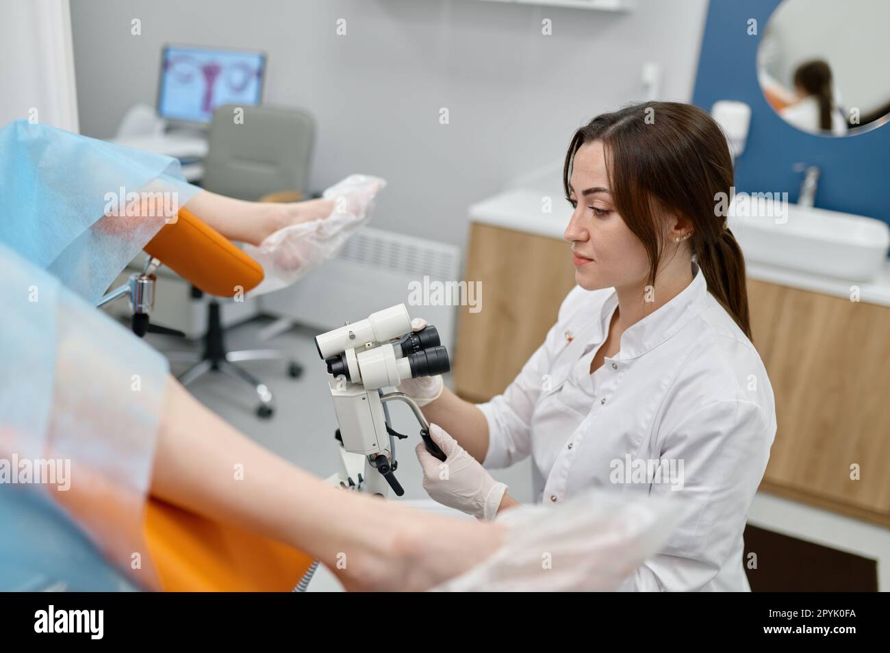 Ginecologo che esamina il paziente su sedia con microscopio ginecologico Foto Stock