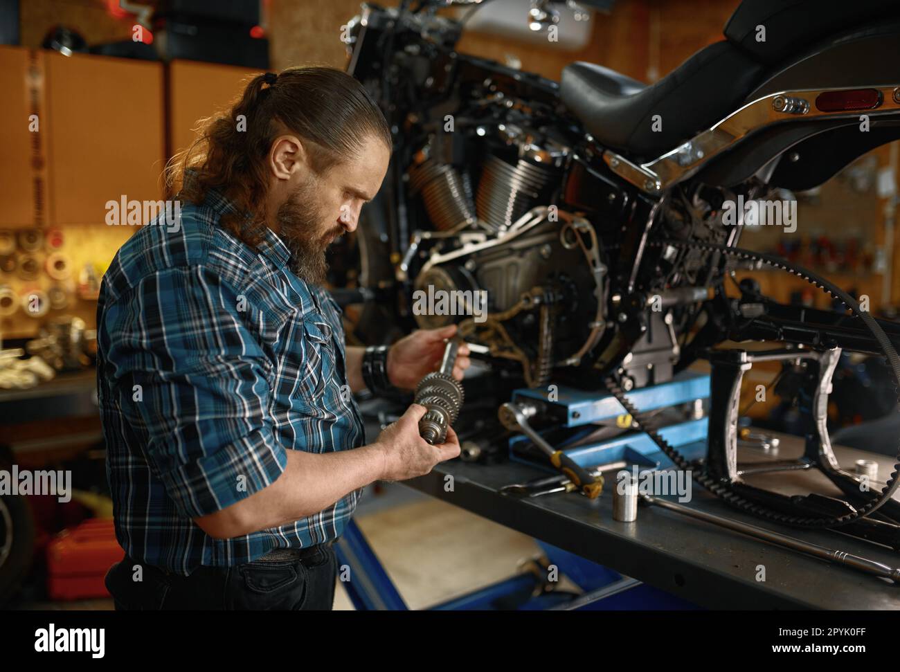 Biker riparatore che guarda il ricambio nel suo e mentre lavora in garage Foto Stock