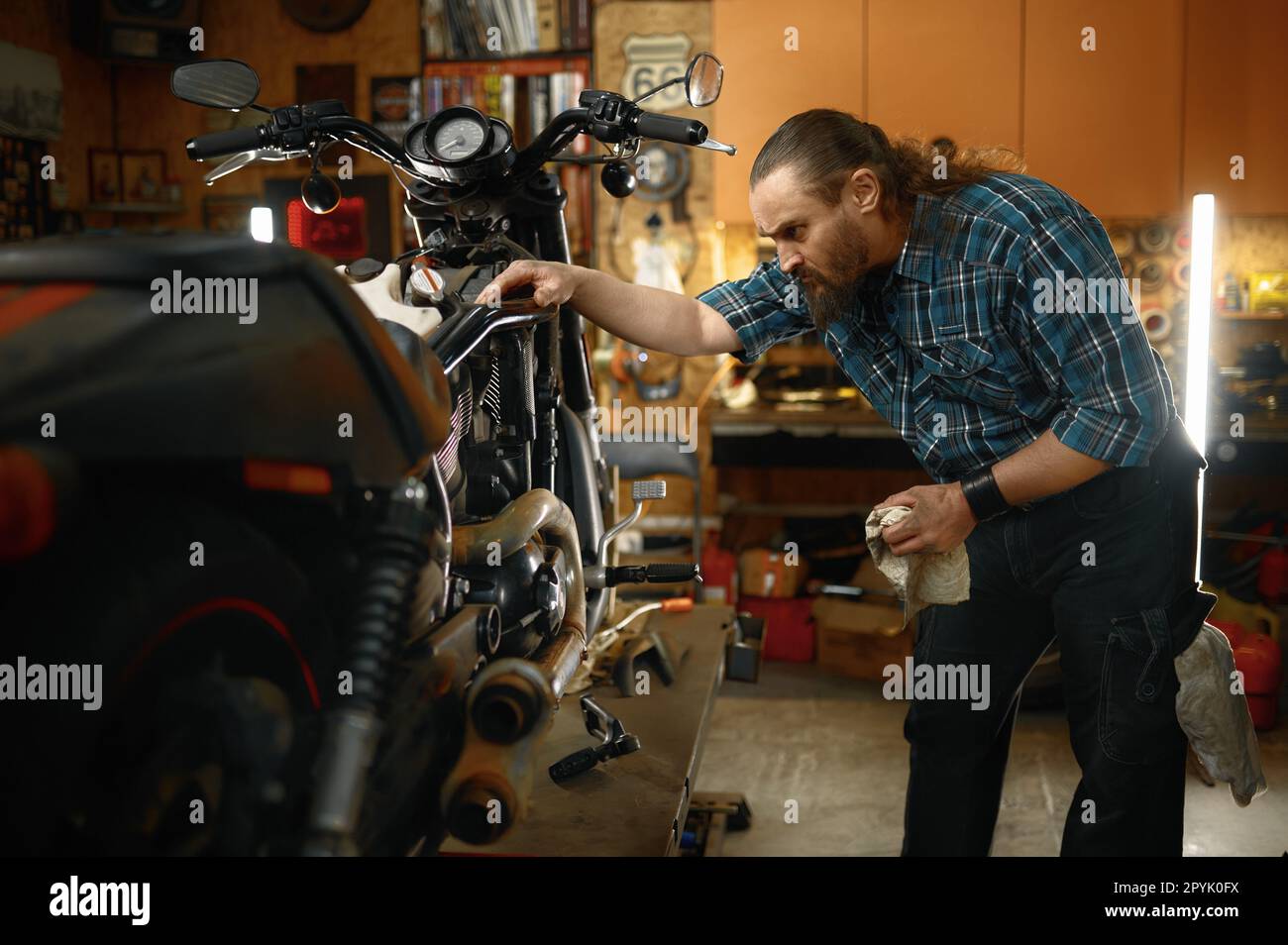 Uomo barbuto biker che lavora nel negozio di riparazione moto il fine settimana Foto Stock