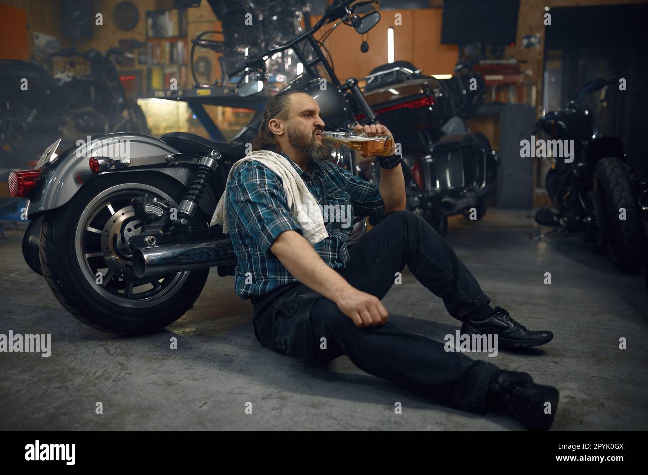 Uomo stanco biker bere birra dalla bottiglia dopo duro lavoro di riparazione in garage Foto Stock