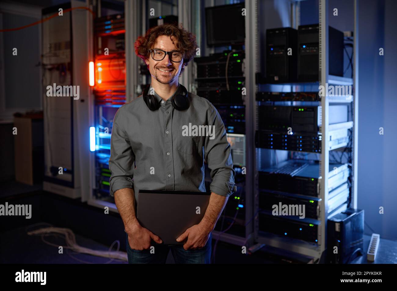 Ritratto di un tecnico di rete sorridente in piedi con un computer portatile nella sala server Foto Stock