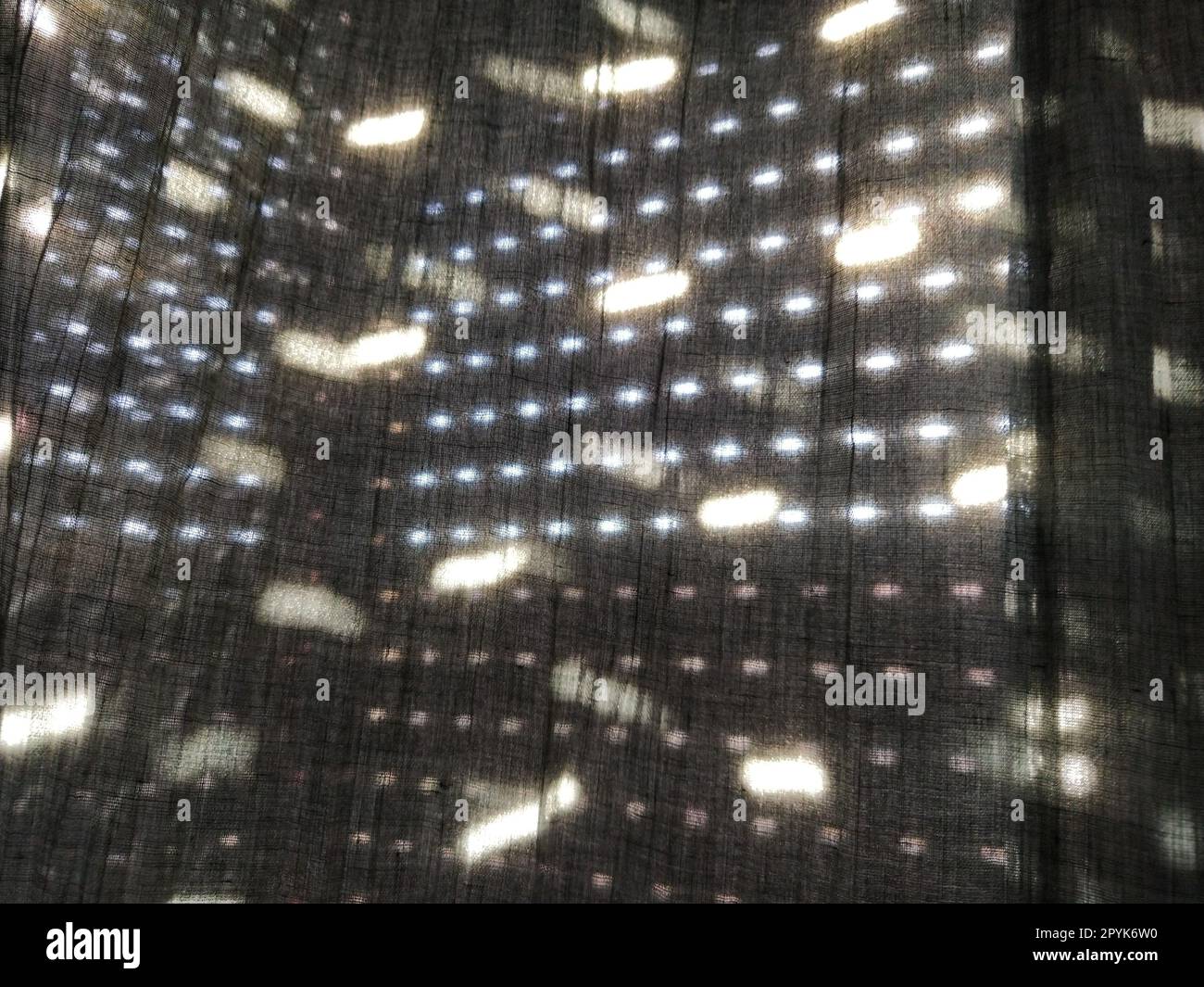La luce del sole splende attraverso tende con piccoli fori e tende grigie - tulle. Immagine astratta. Atmosfera estiva. Riflessione dei punti luminosi sul tessuto Foto Stock