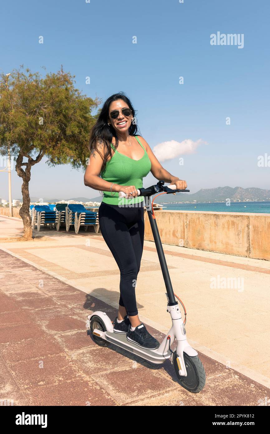 Donna in scooter elettrico, felice ed estivo giro in un resort sulla spiaggia dell'isola tropicale per le vacanze. Città, strada e trasporto ecologico, divertimento su escooter in vacanza a maiorca, isola delle baleari Foto Stock