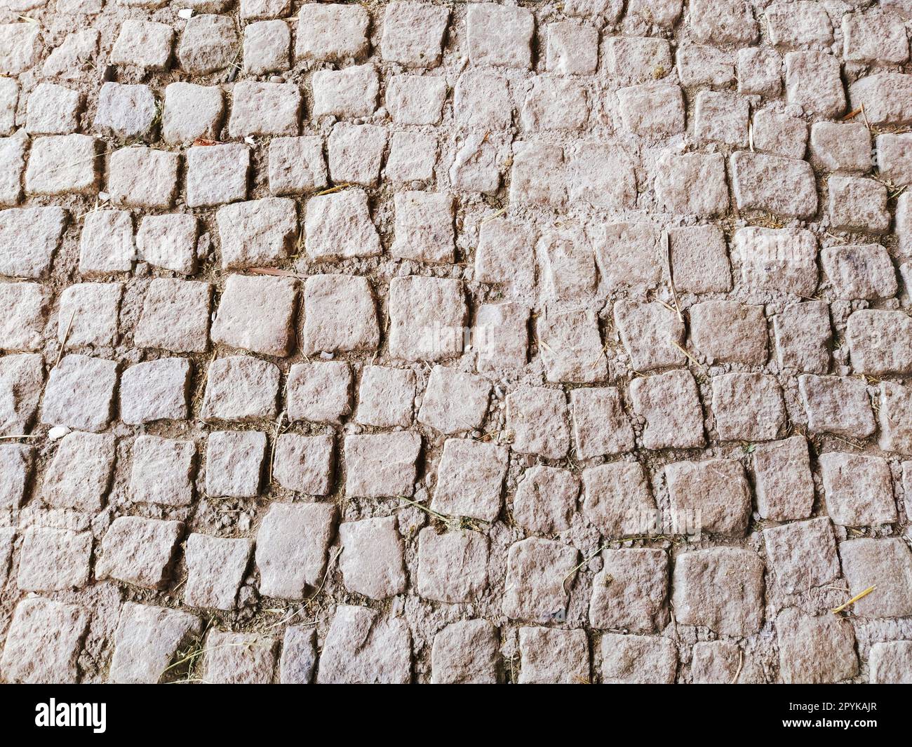 pavimentazione pavimentata con pietre naturali irregolari. Tra i ciottoli schiacciati ci sono piccoli ciottoli, terra, sabbia, erba. Piazza nella città vecchia europea. Foto Stock