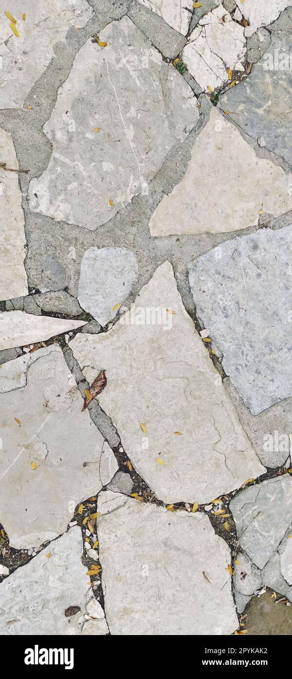 pavimentazione pavimentata con pietre irregolari di colore grigio naturale e marrone. Tra i ciottoli frantumati ci sono piccoli ciottoli, terra, sabbia, erba. Illuminazione solare. Nella vecchia città europea Foto Stock