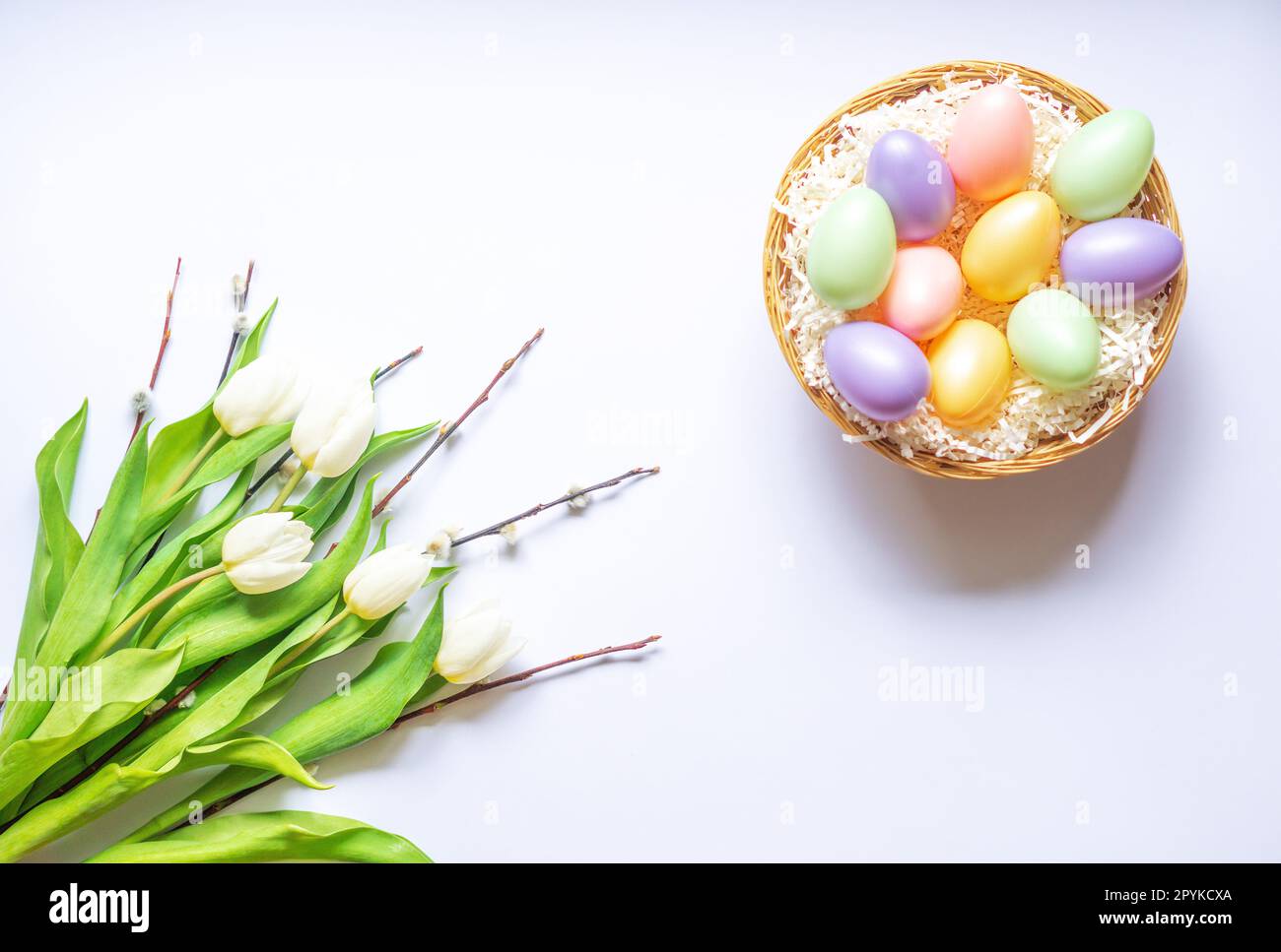 Uova di Pasqua colorate in un cestino. Bouquet di tulipani bianchi e rami di salice. Sfondo. Foto Stock