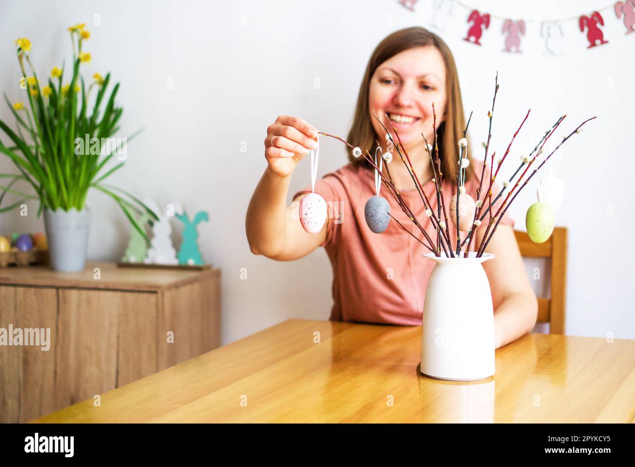 Sorridente bella donna decorando un bouquet di rami di salice con uova di Pasqua colorate a casa. Foto Stock