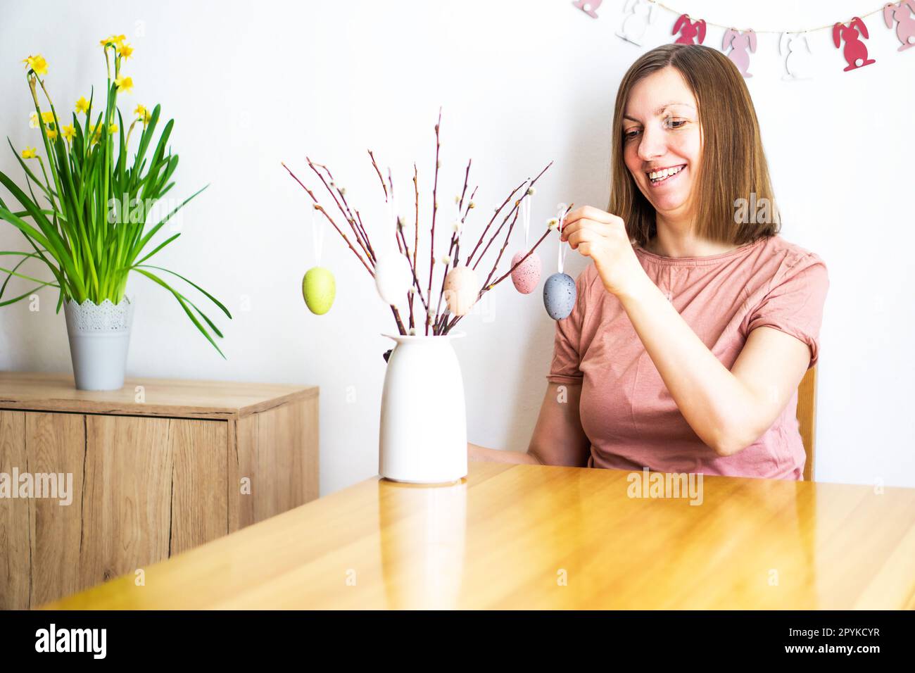 Donna sorridente che decora un bouquet di rami di salice con uova di Pasqua colorate a casa. Buona Pasqua Foto Stock