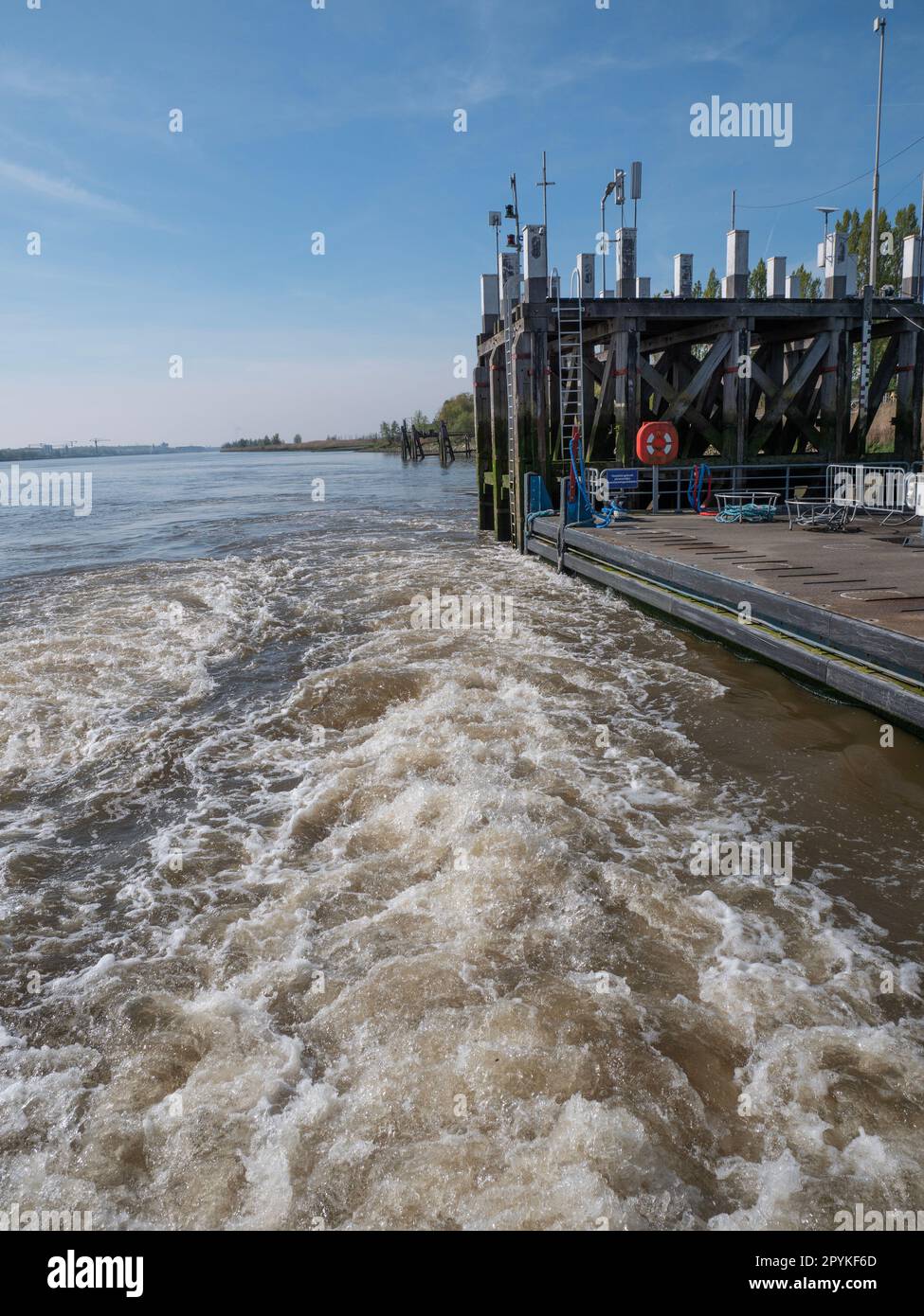 Acqua vorticosa da una barca in partenza su un fiume con il molo sullo sfondo Foto Stock