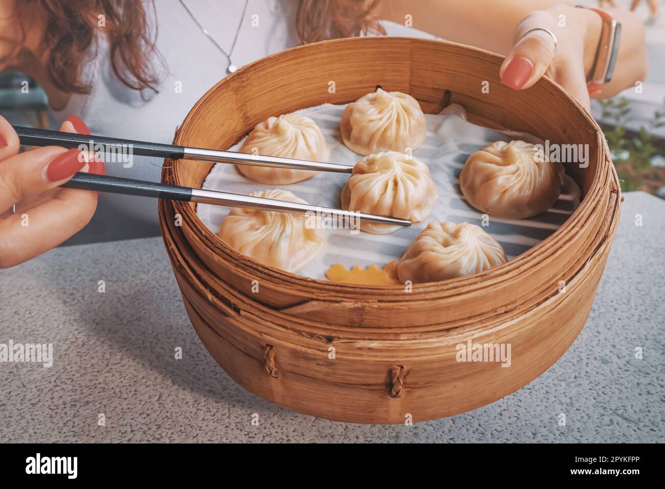 Ragazza con bacchette che prova deliziosa, prelibatezza tradizionale cinese, gnocchi Xiaolongbao, o baozi buns presentato in un piatto di bambù per un autentico Foto Stock