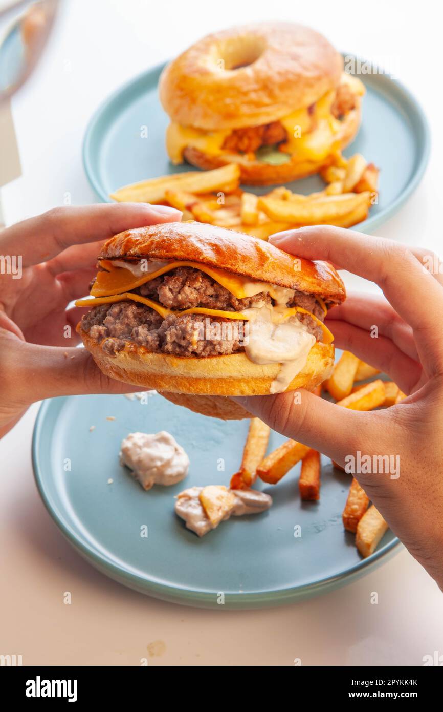 Hamburger di manzo con polpette schiacciate e brioche ciambella in mano. Foto Stock