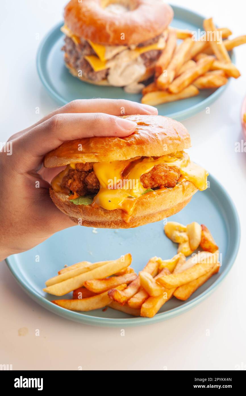 Hamburger di pollo fritto con brioche ciambella e patatine fritte in una mano. Foto Stock