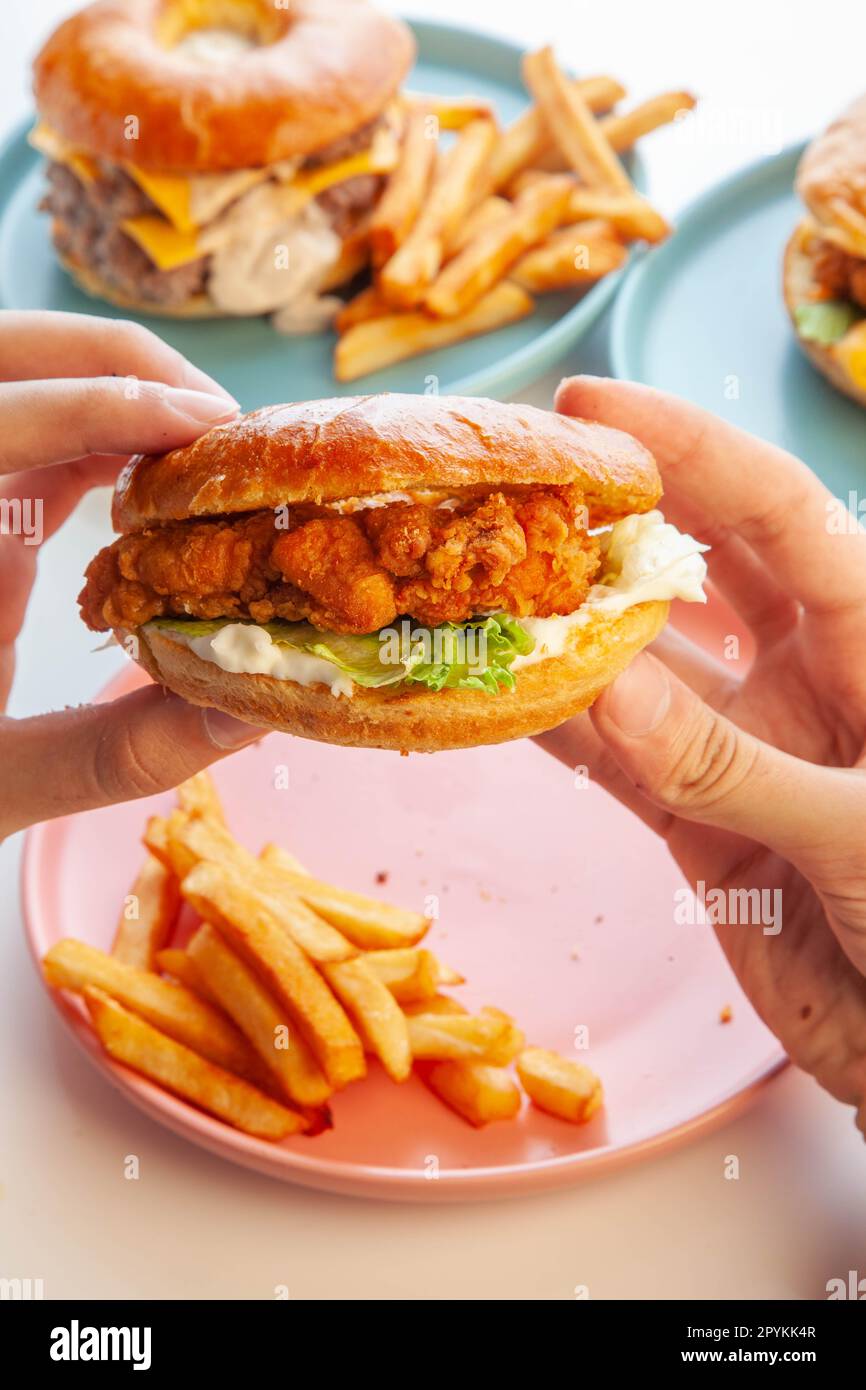 Hamburger brioche di pollo fritto e croccante servito con patatine fritte tagliate a mano su piatto rosa. Foto Stock