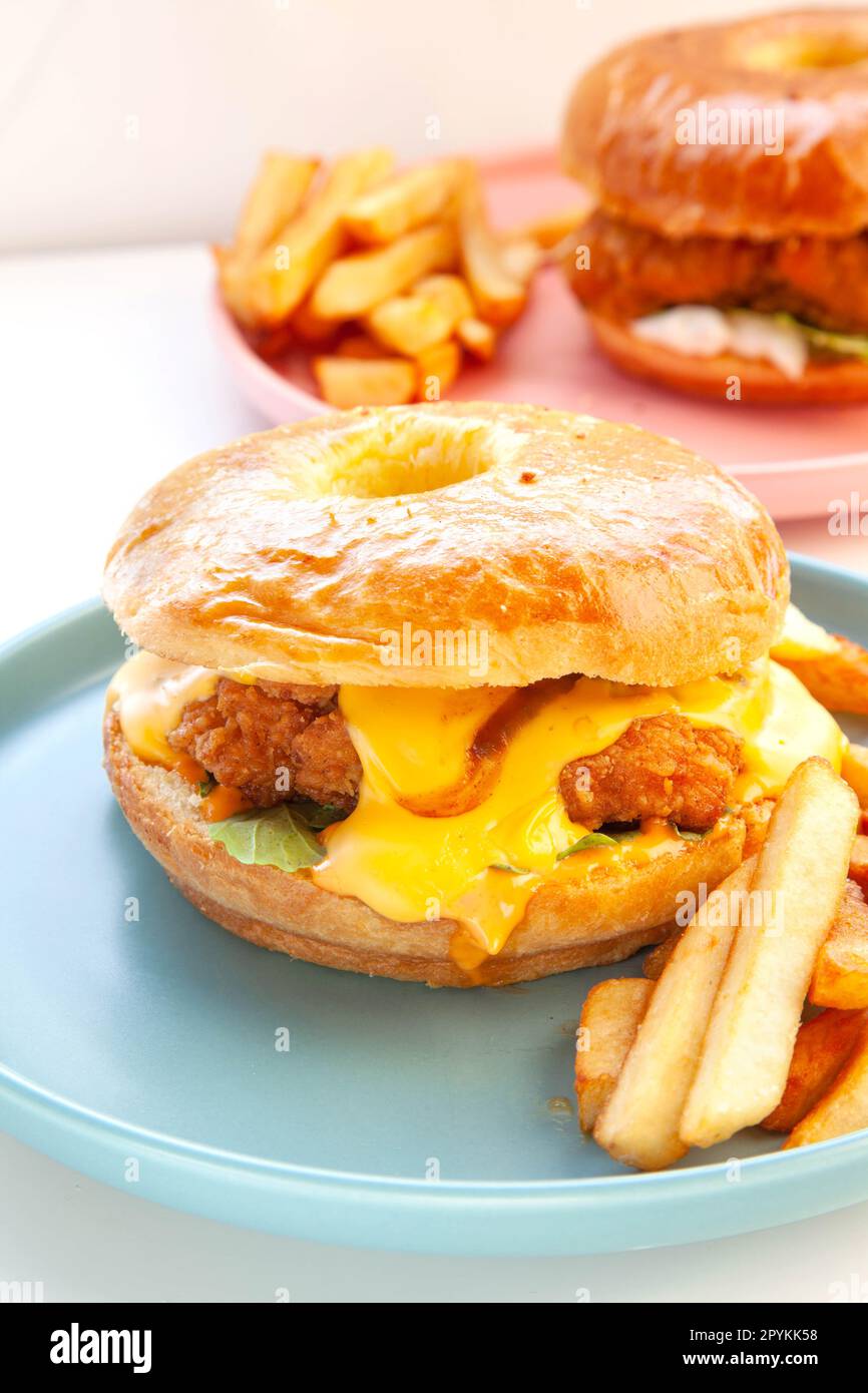 Hamburger di pollo fritto con brioche ciambella e patatine fritte in una mano. Foto Stock