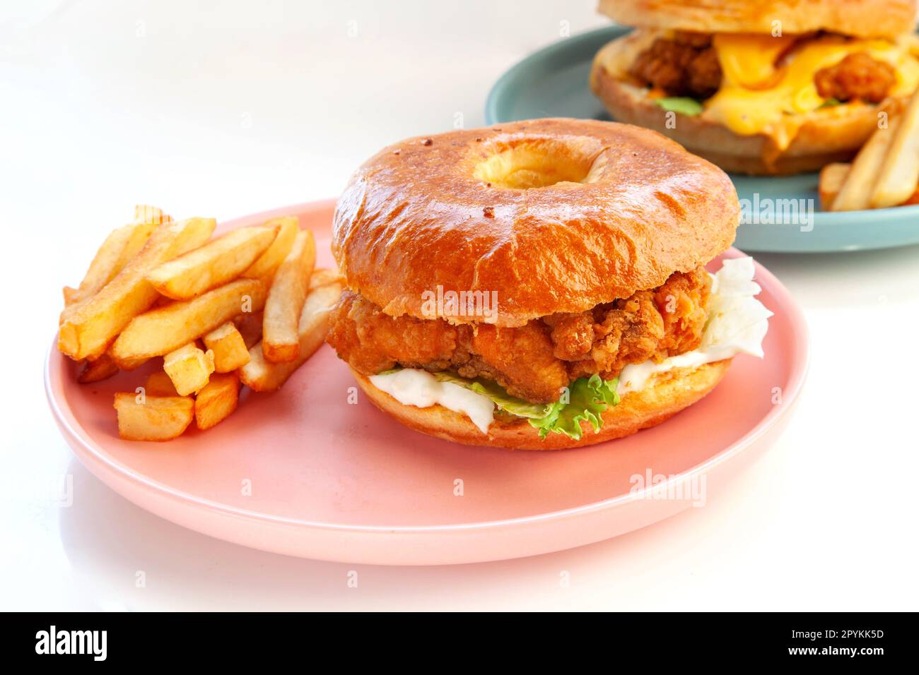 Hamburger brioche di pollo fritto e croccante servito con patatine fritte tagliate a mano su piatto rosa. Foto Stock