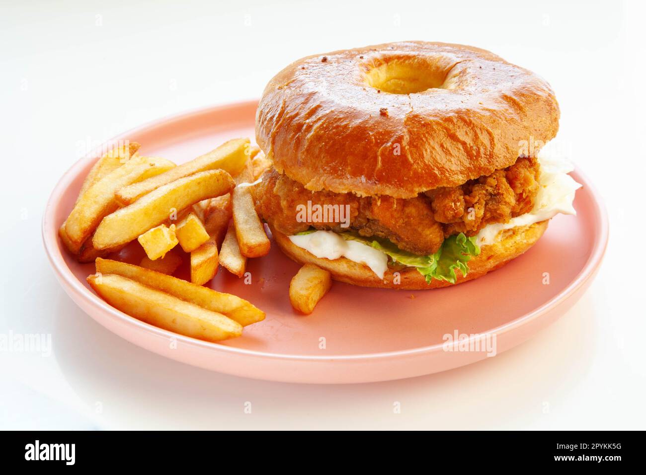 Hamburger brioche di pollo fritto e croccante servito con patatine fritte tagliate a mano su piatto rosa. Foto Stock