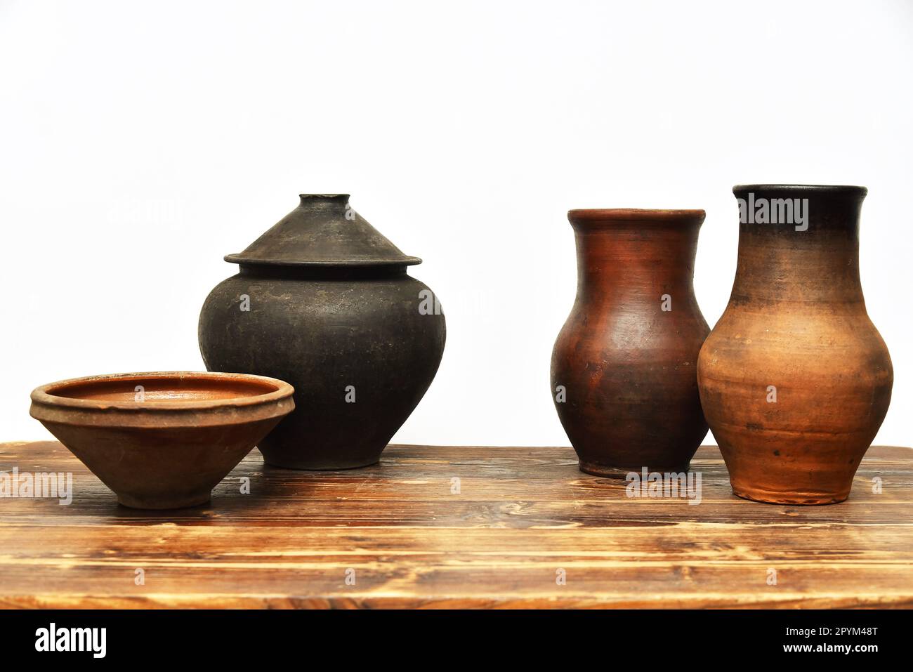 Vasi, ciotole e brocche di terracotta vintage su un tavolo di legno su sfondo bianco. Set di caraffa, ciotola e pentole Foto Stock
