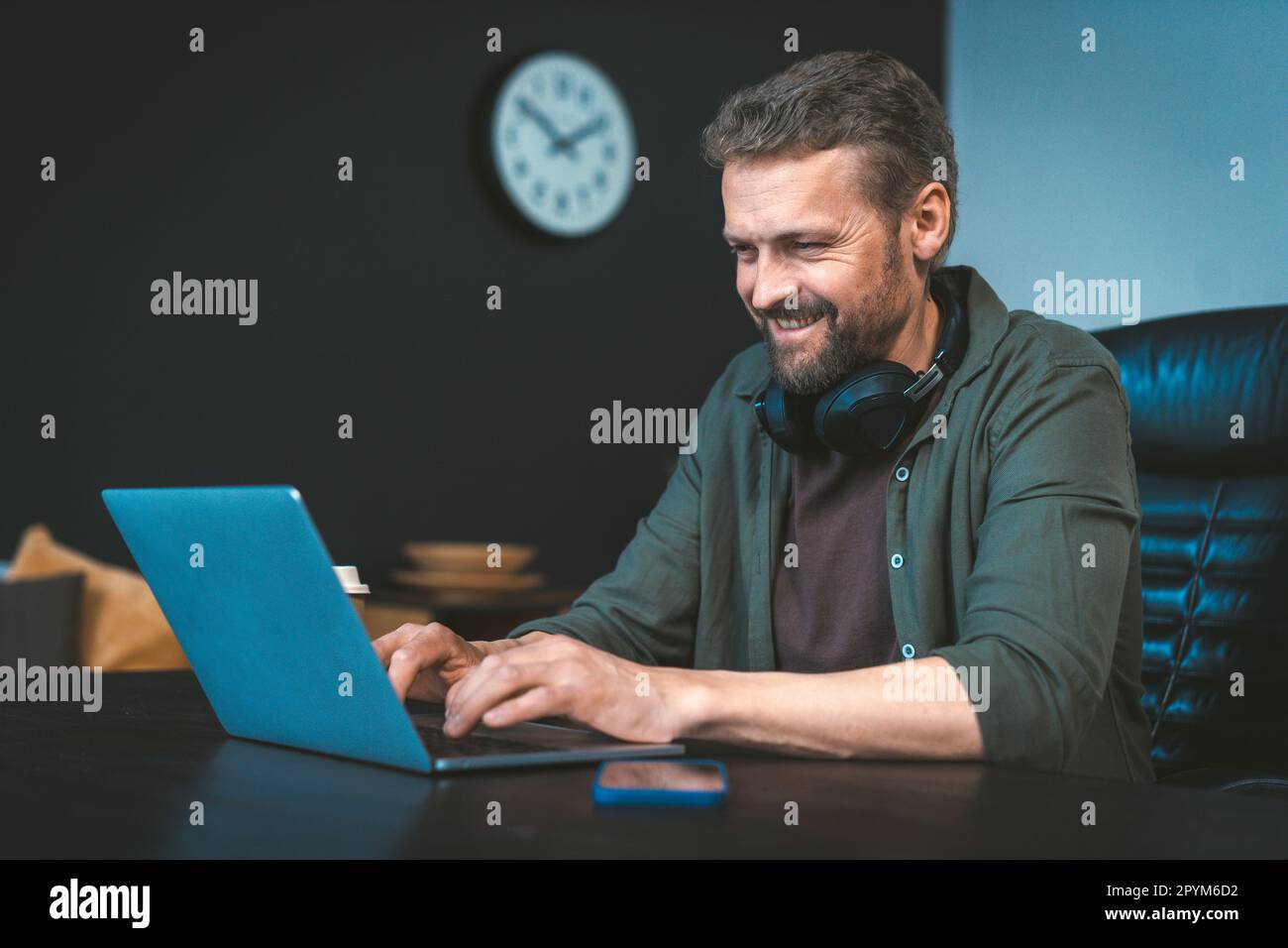 Un uomo felice e motivato lavora su un computer portatile alla scrivania in un elegante ufficio loft, con l'intenzione di fare soldi. Si è concentrato e determinato, ma anche rilassato e confortevole in un ambiente di lavoro. Foto di alta qualità Foto Stock