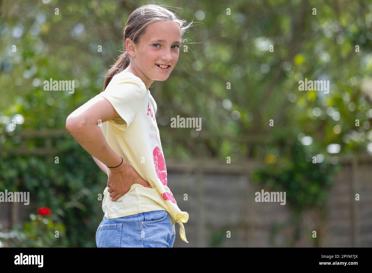 Giovane ragazza in piedi nel giardino sorridente, Little Waltham, Essex, Inghilterra Foto Stock